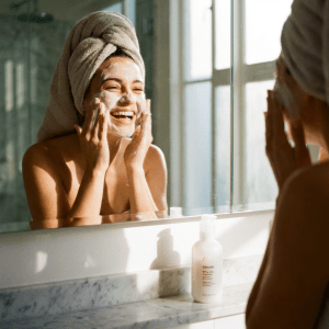 Woman washing face with foaming cleanser in bathroom mirror